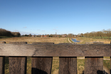 Scenic view of a tranquil landscape with a river, fields, and distant houses under a clear blue sky in a rural setting
