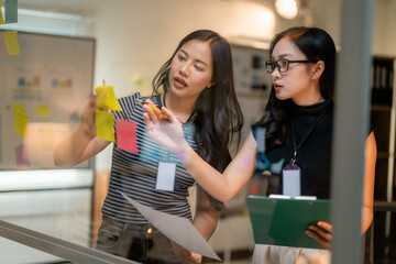 Businesswomen planning strategy using sticky notes on glass wall in office