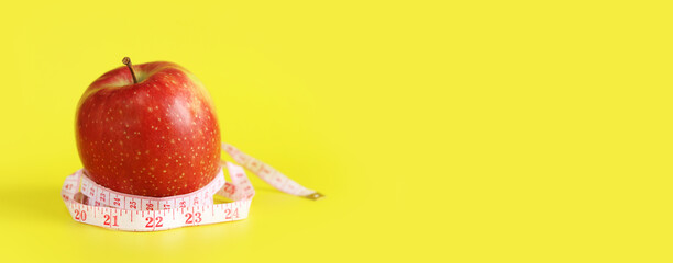 Measuring tape wrapped around apple on yellow background. Healthy eating and weight loss concept. Composition with white measuring tape and apple. Diet. Healthy lifestyle