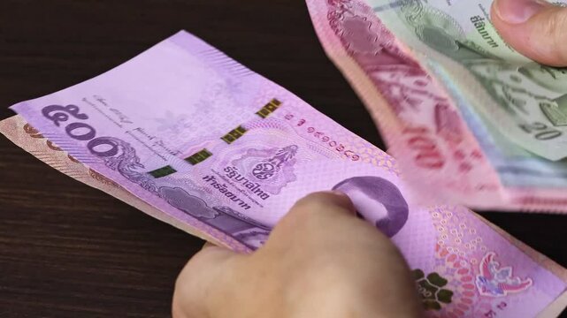 Close up view of woman's hands counting Thailand currency notes (THB). Thailand cash money of 1000, 500, 100, 50 and 20 baht denominations. Real time motion video.