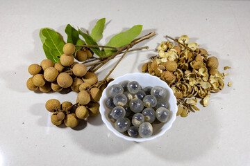 Clusters of longan fruits rest beside a bowl filled with translucent mucilage, while dried peels are scattered nearby, showcasing the fruit's tropical essence and culinary potential.