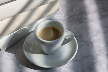 A white cup of espresso on the table with white books beside it, seen from the side. A cup of espresso on the table. 