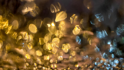 Yellow bokeh effect in night or evening street lighting on car glass in frost. Winter abstract background. A drop of water on the window. The lights are out of focus.