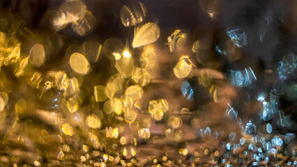 Yellow bokeh effect in night or evening street lighting on car glass in frost. Winter abstract background. A drop of water on the window. The lights are out of focus.