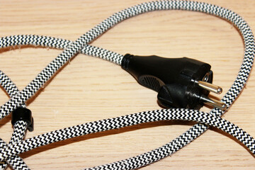 Close-up of an electrical plug and cord with black and white pattern lying on wooden surface