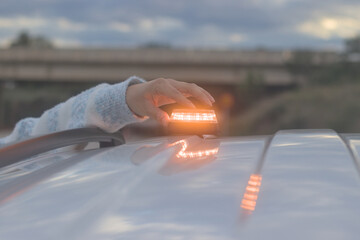 Hand placing a V16 emergency beacon on the roof of a broken-down vehicle. The emergency flasher is mandatory for replacing triangles in Europe. DGT Spain.