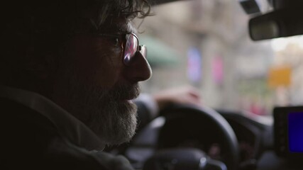 Experienced professional driver with glasses and beard carefully maneuvers through urban traffic, demonstrating focus and expertise behind the wheel of a contemporary car