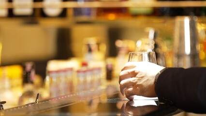 Closeup customer hand in suit with gin fizz or tonic soda at luxurious bar side view in atmosphere at bokeh lighting warm nightclub. Lifestyle with friends or couple at pub and restaurant. Vinosity.