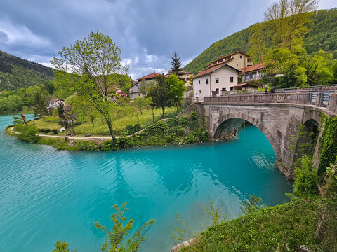 Turquoise soča river meandering under stone arch, flowing past verdant landscape with traditional slovenian village nestled among rolling emerald hills
