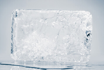 Natural melting textured ice block with cracks on a white reflective surface.