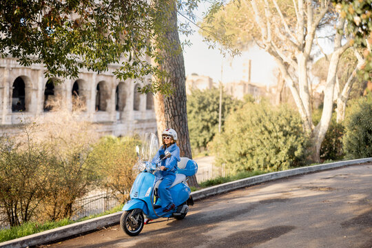 A fashionable woman in a blue outfit and helmet rides a scooter near the iconic Colosseum in Rome, Italy. The image captures the essence of Italian lifestyle, freedom, and elegance on two wheels