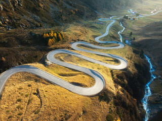Aerial view of winding mountain road, river in alpine valley at sunset in autumn. Top view of road...