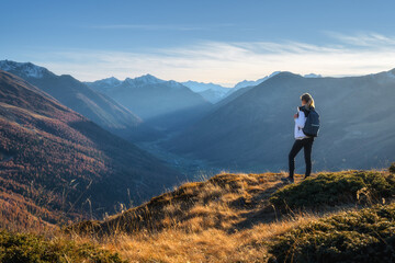Young woman with backpack standing on grassy mountain ridge enjoying inspiring view of valley with...