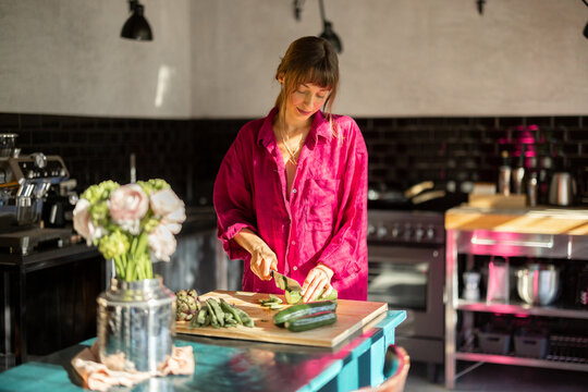 A woman in a relaxed home atmosphere prepares fresh vegetables on a rustic wooden table, bathed in warm natural light. A representation of slow living, wellness, and mindful daily rituals