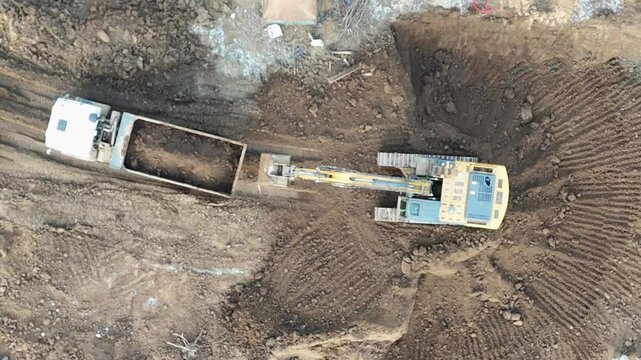 A large construction vehicle is pulling a trailer with a large bucket on the back. The bucket is filled with dirt and rocks. The scene is a construction site, and the vehicle is likely a bulldozer
