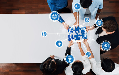 A diverse team collaborates over a table, focused on a puzzle piece globe with digital icons. This image represents teamwork, strategy, and modern business solutions. Amity