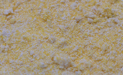 Close-up of yellow corn flour, background of white flour with particles, top view angle