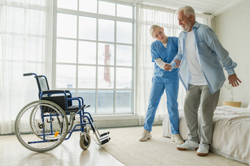 Rehabilitation healthcare. Physiotherapist nurse helps old man patient in wheelchair stand up...
