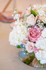 A wedding table centerpiece sits pretty in a gold compote bowl. The arrangement features white roses, ranunculus, and pastel carnations