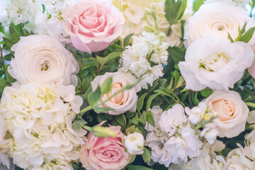 A wedding table centerpiece sits pretty in a gold compote bowl. The arrangement features white roses, ranunculus, and pastel carnations