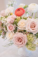 A wedding table centerpiece sits pretty in a gold compote bowl. The arrangement features white roses, ranunculus, and pastel carnations