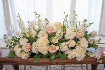 A wedding table centerpiece sits pretty in a gold compote bowl. The arrangement features white roses, ranunculus, and pastel carnations