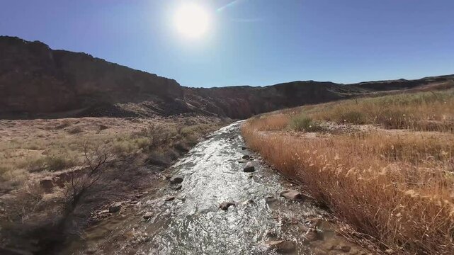 Virgin River Gorge- Hurricane, Utah, USA - February 10, 2025: Aerial-FPV-First Person View-Flying low over shallow rocky river bed with climb out to reveal valley beyond-Blue sky and sun flare