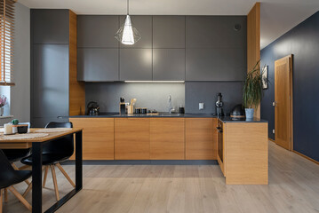 Modern kitchen interior with kitchen furniture, wooden cabinets, counter and dining table with black chair. Luxury and Design room at new home. Real estate.