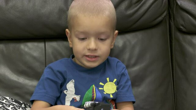 Child playing with new toy sitting on sofa at home. Concentrated face of little boy holding transformer robot toy. Three year old child examining new toy comments on his actions.