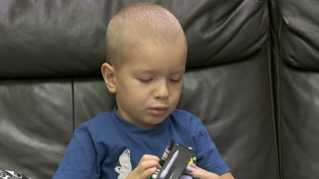 Child playing with new toy sitting on sofa at home. Concentrated face of little boy holding transformer robot toy. Three year old child examining new toy comments on his actions.