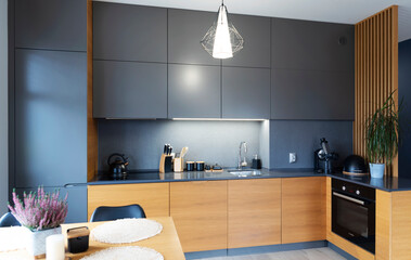 Modern kitchen interior with kitchen furniture in dark colour, wooden cabinet, oven and kitchen sink with tap. Home design in new apartment with dining table and chair. 