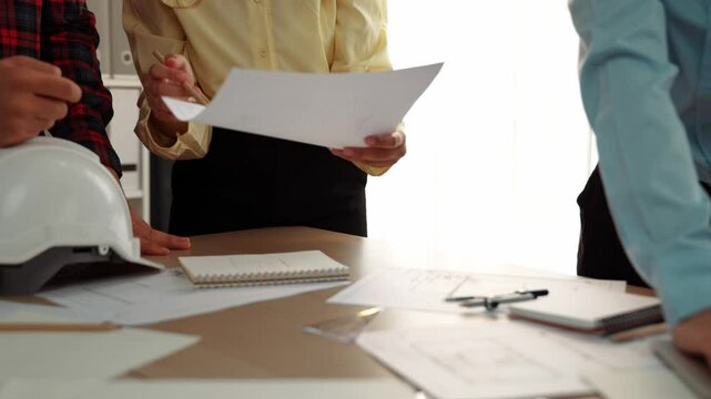 Architect and safety engineer discussion about building blueprint displaying on laptop on table with architectural document and wooden block scatter around at modern office. Closeup. Delineation.