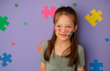 A girl with an autism spectrum disorder on a violet studio background decorated with large multicolor puzzles. Specialized education for special people