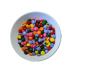 A full bowl of colourful candies top view isolated background. Chocolate buttons sweet treats in white bowl.