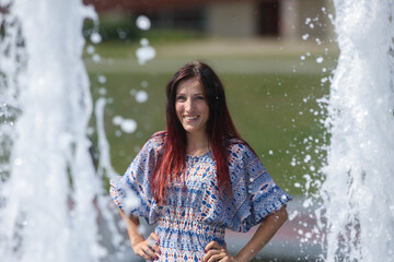 A beautiful young woman poses against the background of a fountain