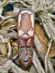 A handcrafted wooden tribal mask with an owl engraving, symbolizing wisdom and mysticism. Placed...