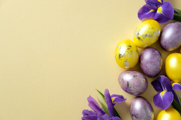 Elegant Easter flat lay composition with golden and purple eggs, vibrant purple irises on a pastel yellow background.