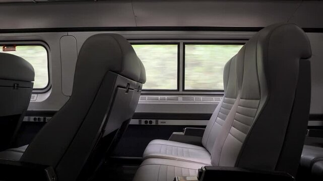 View of empty train seats and landscape passing through a train window.