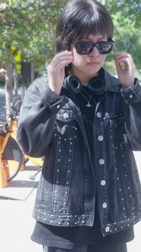 Confident Young Trans Man Adjusting Sunglasses and Using Phone in Urban Setting