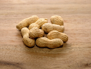 Shelled peanuts lie on a rustic wooden surface, showcasing their textured outer shells. These nuts are often enjoyed as a snack or ingredient in various dishes