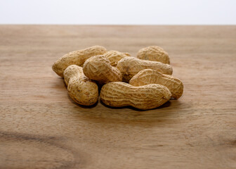 Shelled peanuts lie on a rustic wooden surface, showcasing their textured outer shells. These nuts are often enjoyed as a snack or ingredient in various dishes