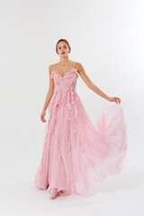 Elegant model showcases a flowing pink evening gown in a minimalist studio setting during a fashion...