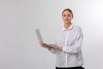 Professional woman confidently holding laptop while posing against a plain background in a modern office setting