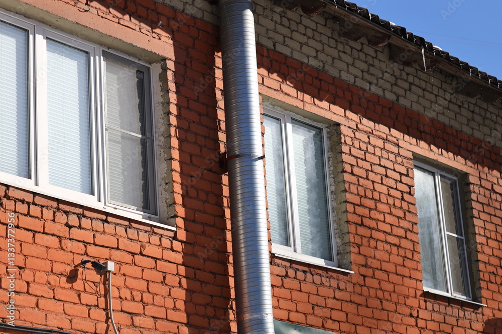 Poster A red brick building with two windows and a metal pipe, suitable for use in urban, architecture or construction images.