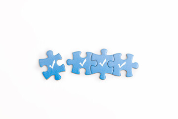 Four blue puzzle pieces with white checkmarks are arranged in a row on white background. represents...