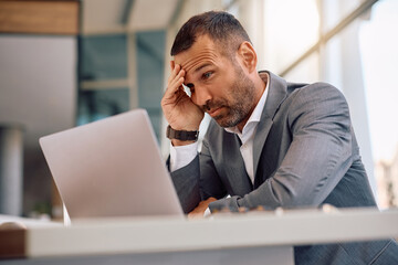 Worried businessman reading problematic email on computer at corporate office.