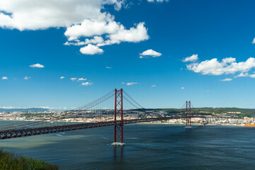25th of April Bridge and Tagus River. Ponte 25 de Abril Suspension Bridge and Lisbon Skyline. Blue Sky and Cumulus Fluffy Clouds. Portugal