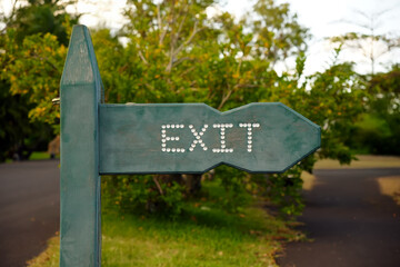 Green wooden exit sign in garden path. Park exit sign with LED dots display. Illuminated exit direction arrow in green park setting