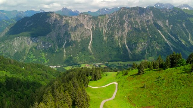 Aerial view of Bavarian Alps near Oberstdorf, Germany, winding mountain road leading to Fellhorn. In foreground majestic mountain range separates Germany and Austria, creating alpine landscape. 