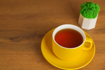 Side view of a yellow cup with saucer in which black tea is poured stands on a wooden table on the left with space for text, next to it is a plant in a white pot. Concept of tea drinking, cleaning